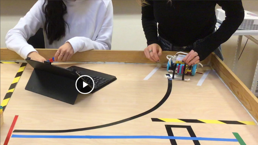 Två elever arbetar med robotprogrammering på en bana av tejp.