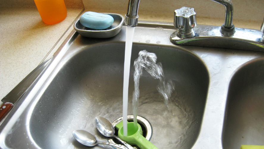 Vatten rinner från en kran ner i en diskho av metall.