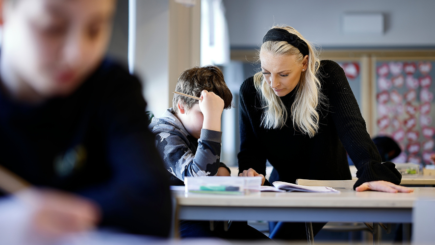 Lärare hjälper elev med uppgift i klassrum. Foto: Peter Holgersson AB.