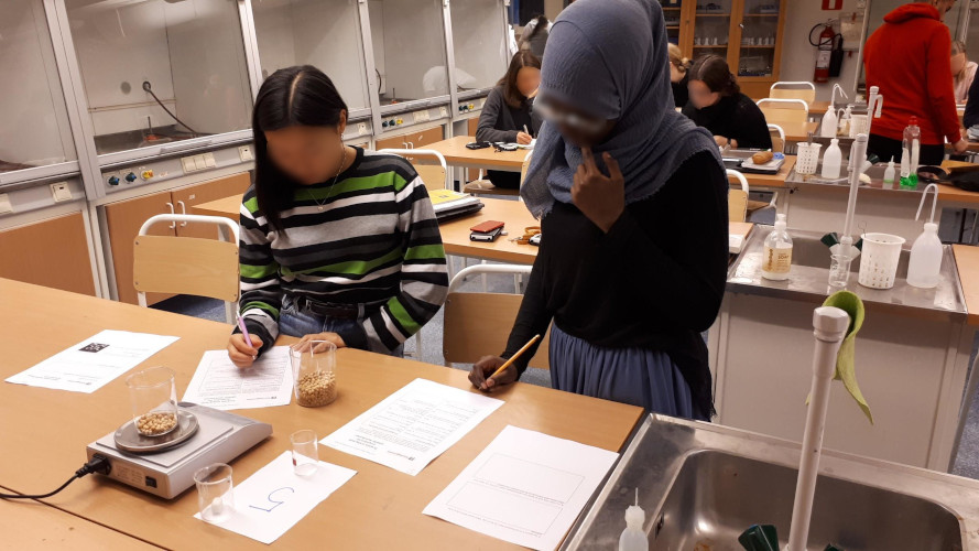Två kvinnliga gymnasielever väger och skriver på papper i en kemisal.