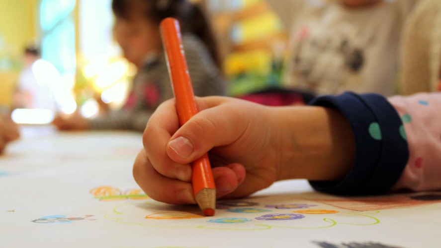 Barnhand ritar med orange penna. 