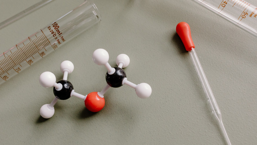 En molekylmodell, ett mätglas och en pipett ligger på en bordsyta.