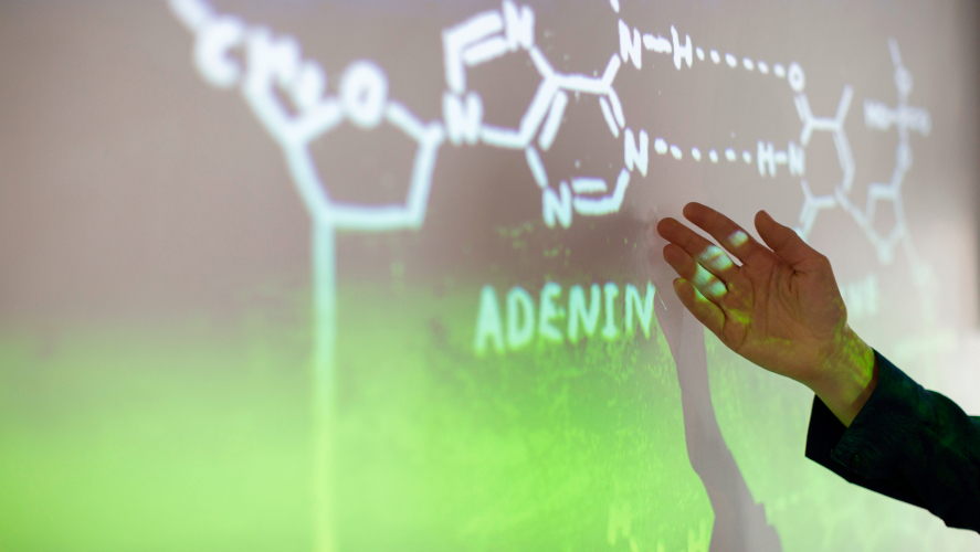 Hand riktas mot en skärm som visar en molekylbild i vitt mot en mörk bakgrund